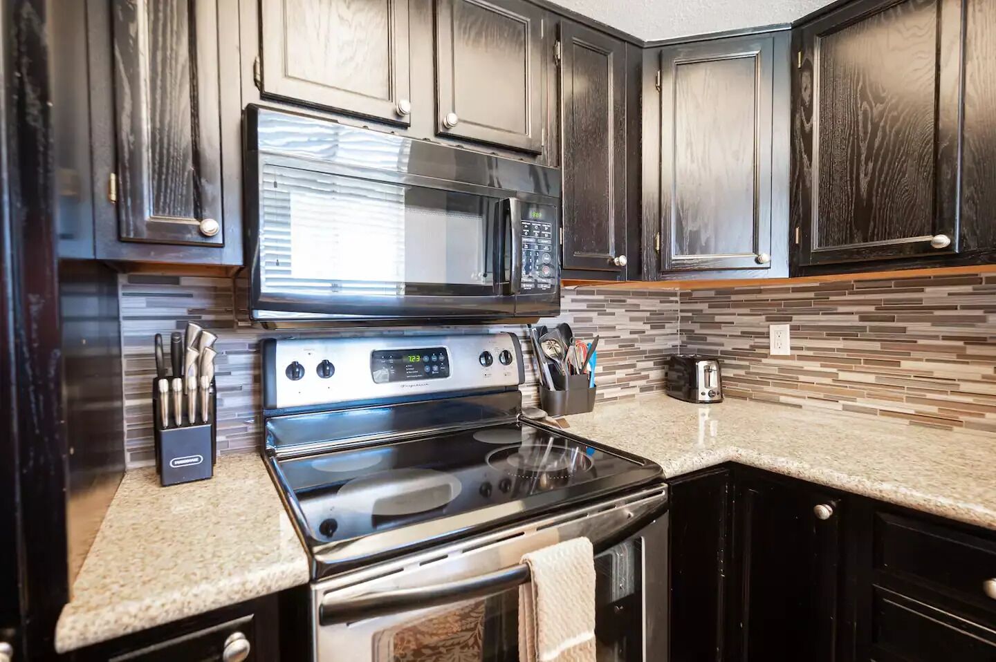 Una cocina con armarios de madera oscura, estufa de acero inoxidable y microondas.