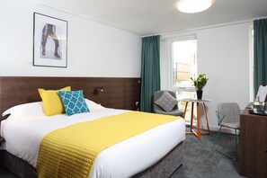 A hotel room with a large bed, a desk, a chair, a window, and a plant. - Sunley Hotel (Northampton)