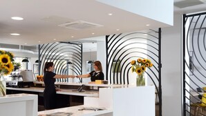 A modern reception area with a white counter, a black and white decorative wall, and a vase with sunflowers. - Sunley Hotel (Northampton)