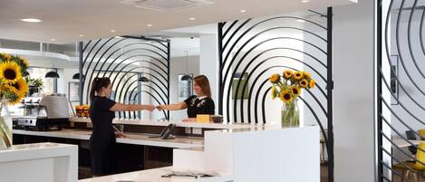 A modern reception area with a white counter, a black and white decorative wall, and a vase with sunflowers.