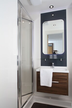 A modern bathroom with a glass shower enclosure, a white sink with a wooden vanity, and a mirror above the sink. - Sunley Hotel (Northampton)