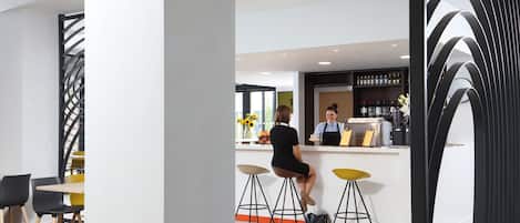 Zona de bar moderna con mostrador, taburetes y una persona sentada.