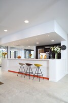 Una zona de bar moderna con una barra blanca, tres taburetes y un reloj en la pared.