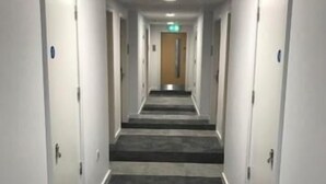 A hotel hallway with carpeted stairs, white walls, and doors with blue signs. - Sunley Hotel (Northampton)