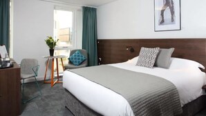 A hotel room with a bed, a desk, a chair, a small table with a plant, and a window with curtains. - Sunley Hotel (Northampton)