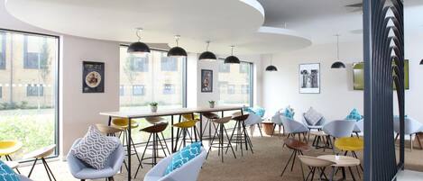 Un espace de restauration moderne avec des tables et des chaises rondes, de grandes fenêtres et des luminaires suspendus.
