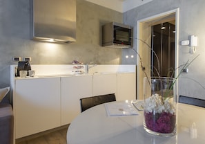 A modern kitchen with white cabinets, a built-in oven, and a glass vase with flowers on the dining table. - Milan Royal Suites Luxury Apartments (MILAN)