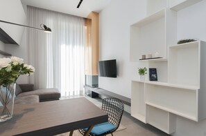 A modern living room with a flat-screen TV, a dining table with chairs, a sofa, and a bookshelf. - Milan Royal Suites Luxury Apartments (MILAN)