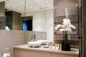 A modern bathroom with two white sinks, a large mirror, and a towel rack with white flowers. - Milan Royal Suites Luxury Apartments (MILAN)