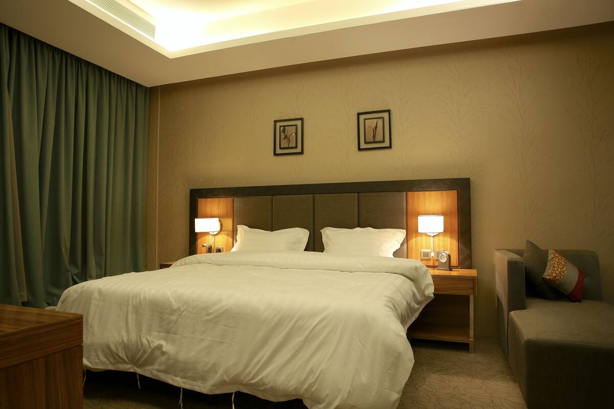 A hotel room with a large bed, two bedside lamps, a wooden nightstand, a chair, and a wall with two framed pictures.