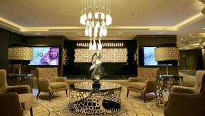 A lobby with a modern chandelier, comfortable seating, and large screens displaying content. - Quetzal (Riyadh)