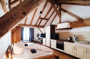 A cozy room with a bed, a desk, a television, and a kitchen area with cabinets and a sink.