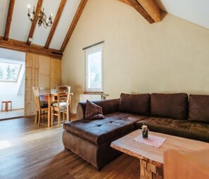 Ein gemütliches Loft-Zimmer mit Holzboden, einem großen braunen Ecksofa, einem Esstisch mit Stühlen und einem Fenster, das natürliches Licht hereinlässt.