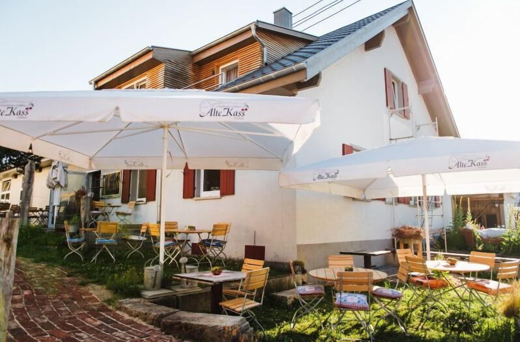 An outdoor seating area with tables and chairs, umbrellas, and a building with a sloped roof in the background.
