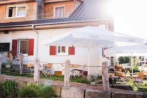 A building with outdoor seating under umbrellas, a wooden fence, and a brick pathway.