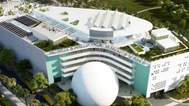Un hotel moderno con una estructura central circular única, varios pisos y abundante vegetación circundante.