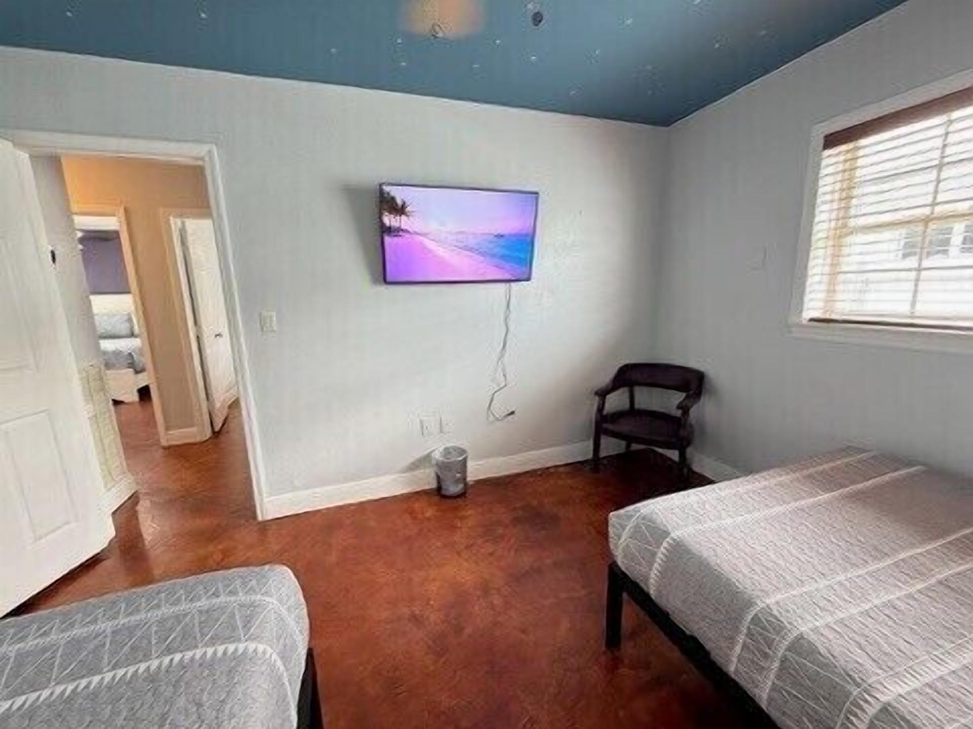 Ein Schlafzimmer mit zwei Betten, einem Fernseher an der Wand, einem Sessel und einem Fenster.