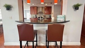 Una cocina con una isla central, dos sillas y lámparas colgantes.