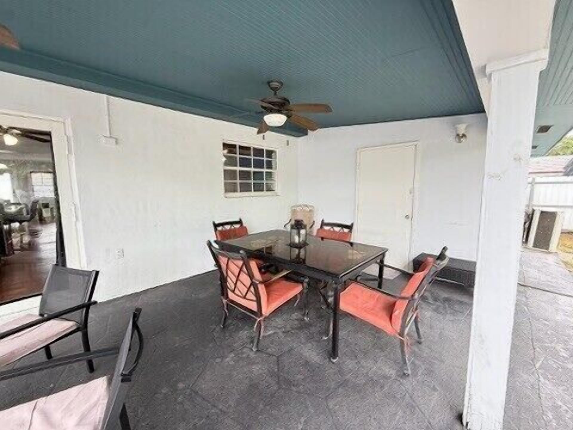 A covered patio with a table and chairs, a ceiling fan, and a door leading to an interior space.