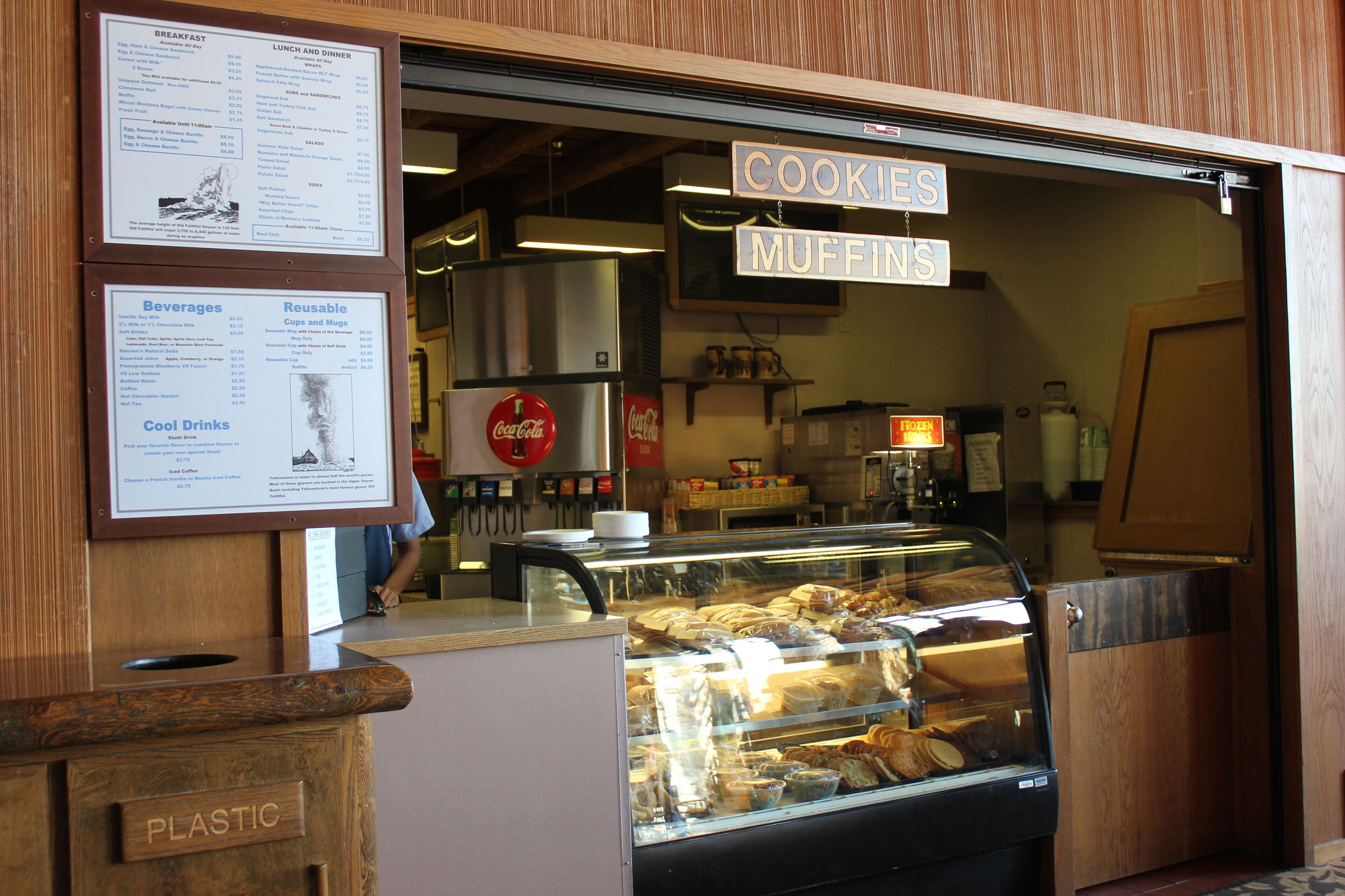 A bakery with a display case of baked goods and signs advertising cookies and muffins.