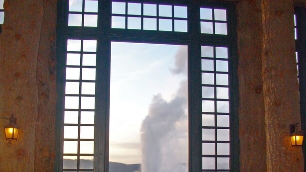 Una habitación con un ventanal grande que ofrece vistas panorámicas. Hay sillas de mimbre y un banco de piedra.