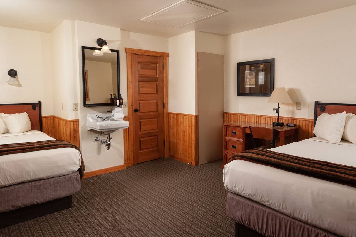 Une chambre d’hôtel avec deux lits, une porte en bois, un lavabo et un bureau avec une chaise.