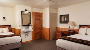 Habitación de hotel con dos camas, una puerta de madera, un lavamanos y un escritorio con una silla.