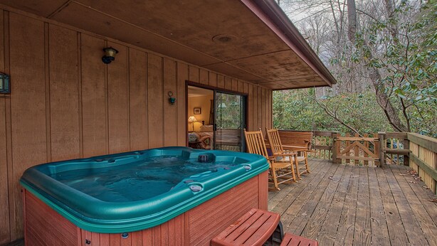 A wooden cabin with a hot tub on the deck, a covered patio with chairs, and a view of trees. - Perfect location, creekside, close to skiing, easy paved access, Game Pavilion! (Maggie Valley)