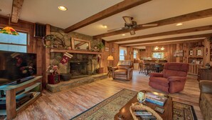A cozy cabin interior with a stone fireplace, leather armchairs, a dining area, and a television. - Perfect location, creekside, close to skiing, easy paved access, Game Pavilion! (Maggie Valley)