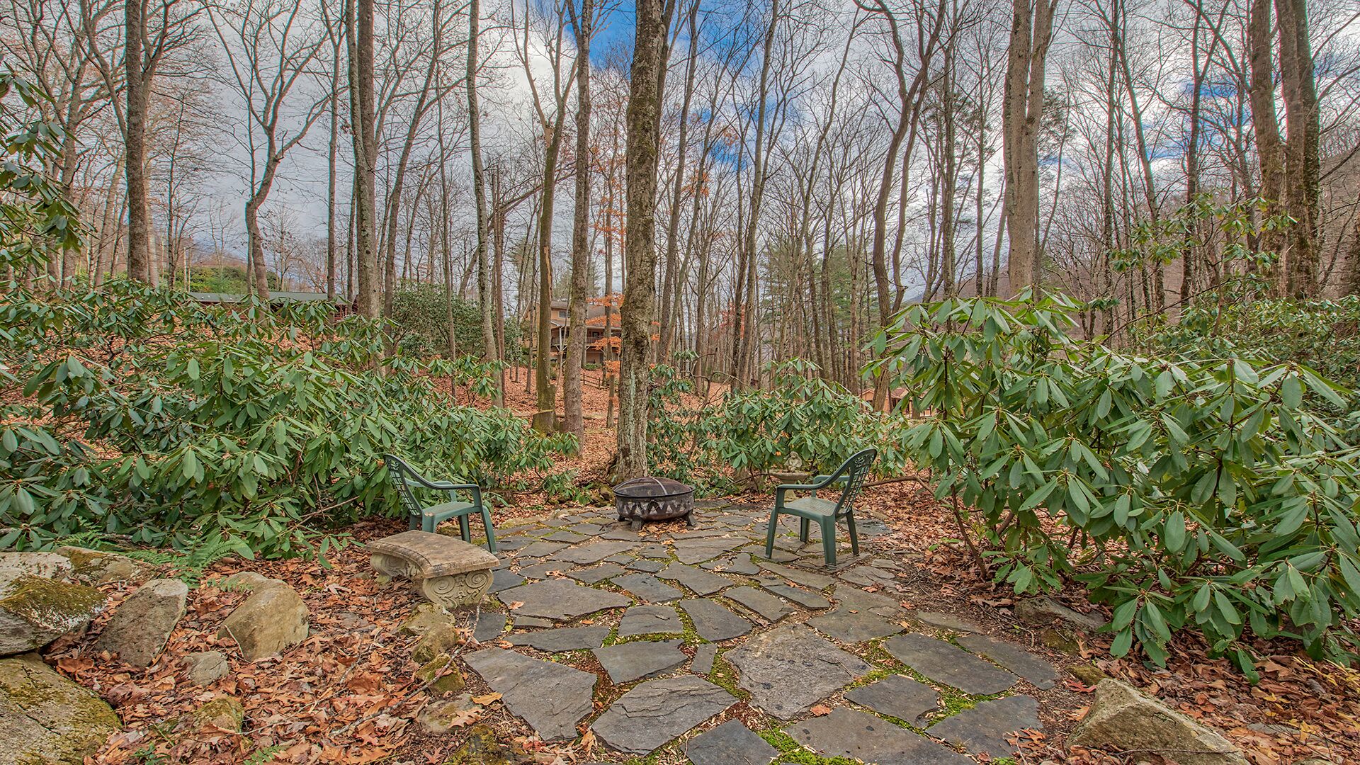 A stone patio with two green benches and a fire pit in a forested area.