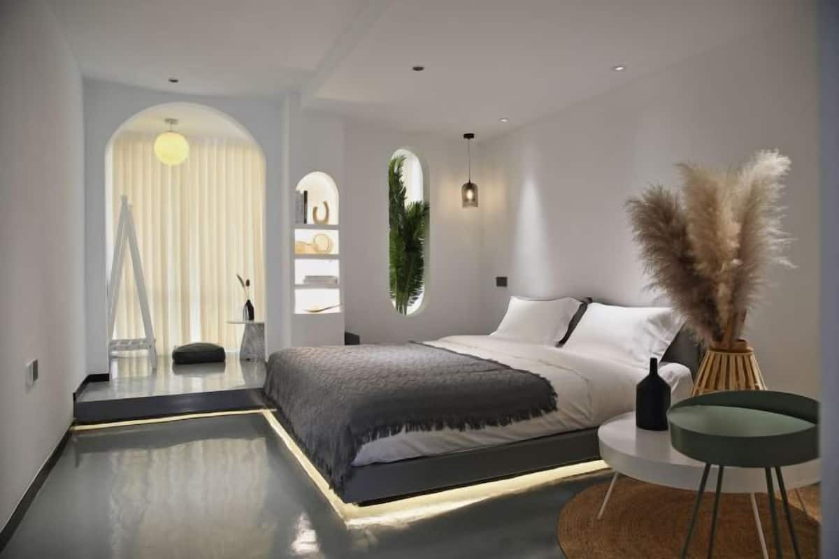 A modern bedroom with a large bed, a round side table, and a small round table with a vase.
