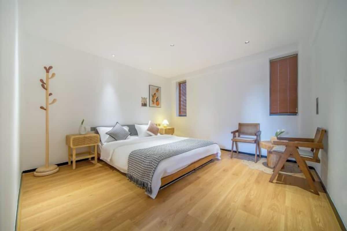 A bedroom with a bed, bedside tables, a floor lamp, a chair, and a window.