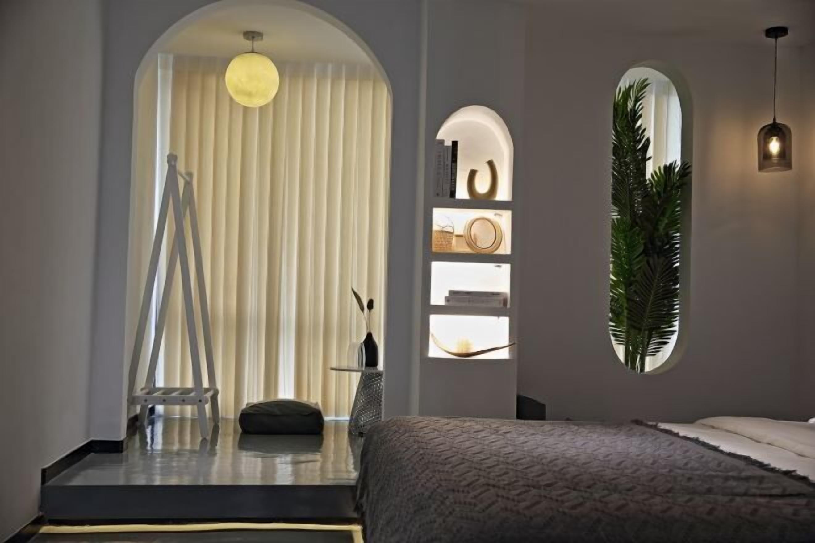 A modern bedroom with a bed, a ladder, a hanging light, and a plant.