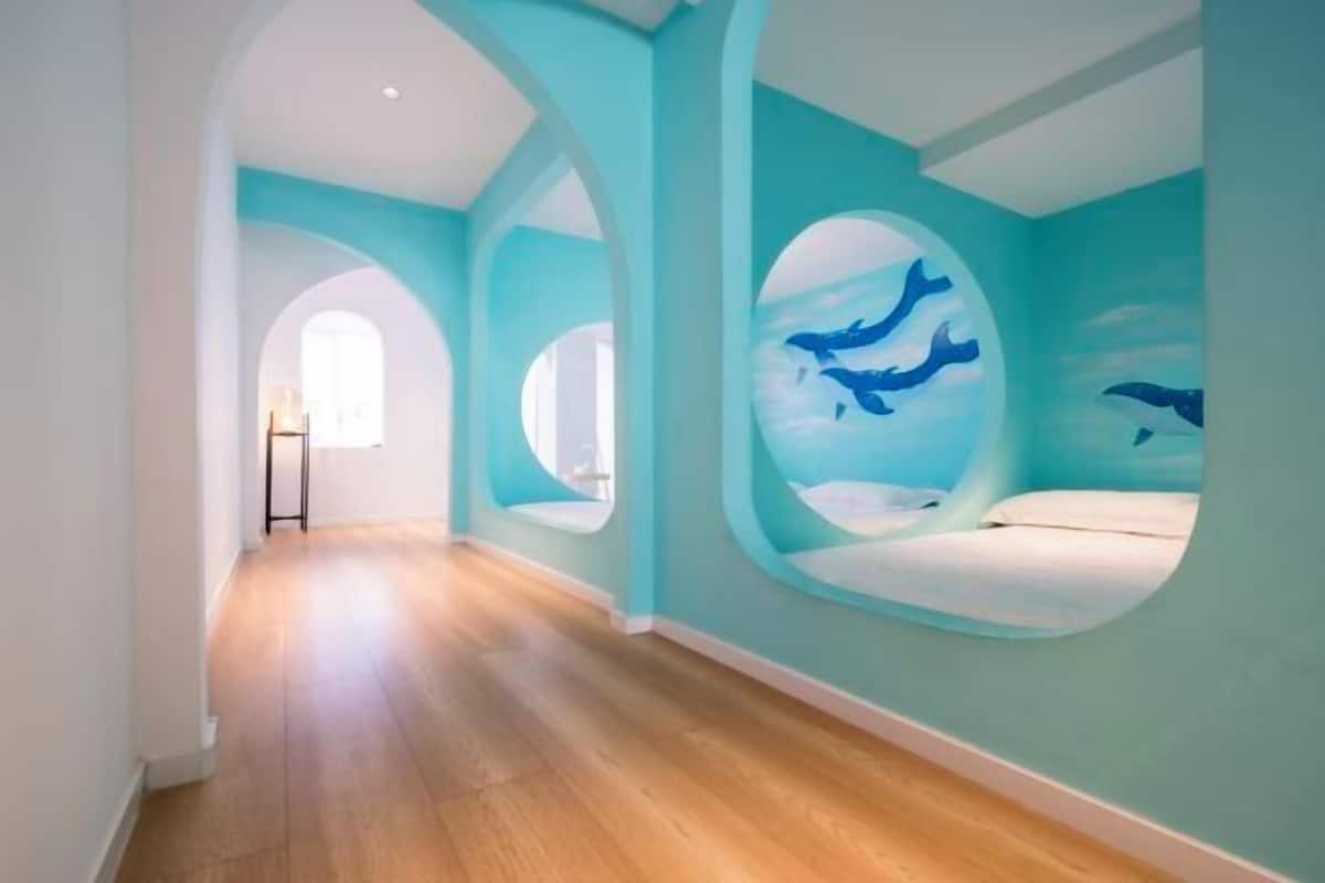 A hallway with a wooden floor, arched doorways, and circular windows with whale paintings.