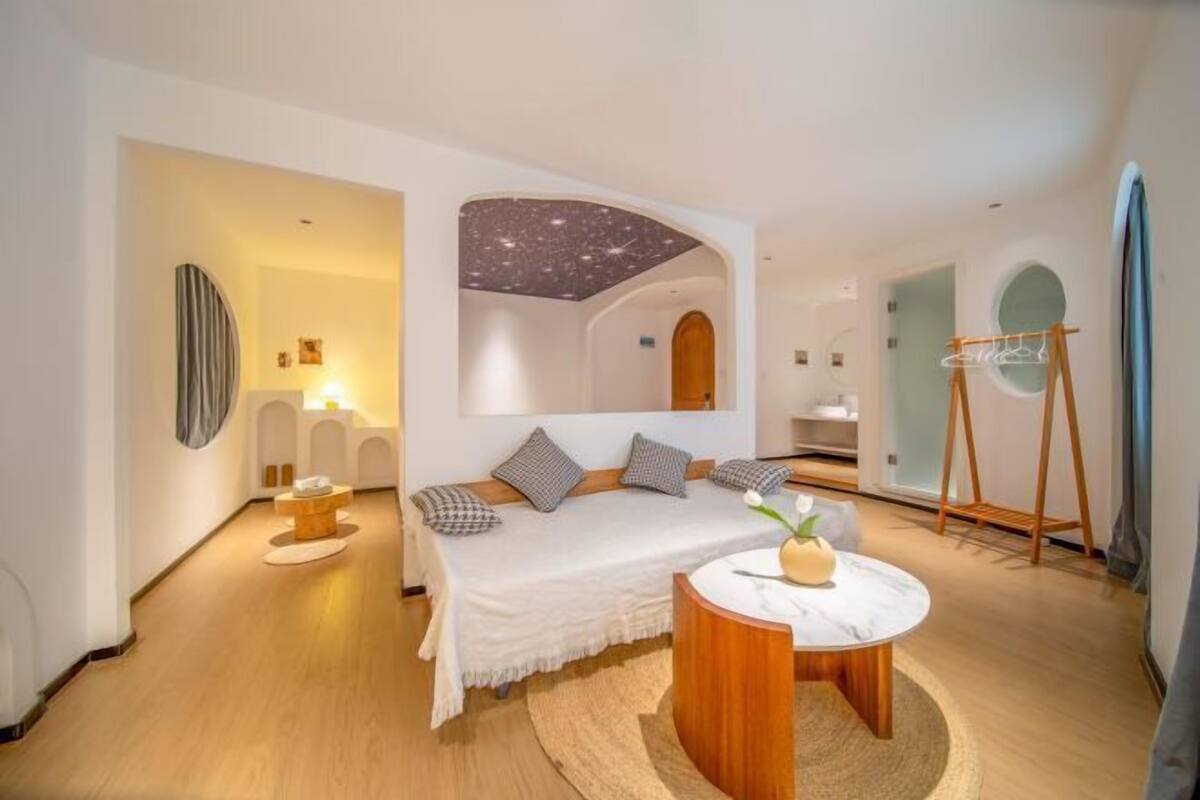 A modern bedroom with a bed, a round wooden table, and a starry ceiling design.
