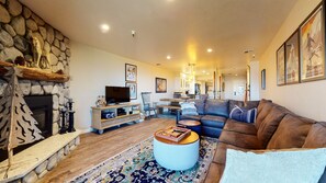 A spacious living room with a stone fireplace, a large sectional sofa, a television, and a dining area with a wooden table and chairs. - Pet-Friendly & Remodeled, Stunning Views. Private Gas Grill & Washer/Dryer (Mammoth Lakes)