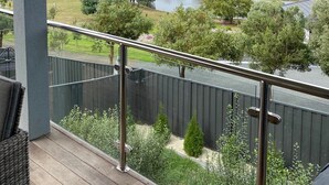 A balcony with a view of a lake, trees, and houses in the distance.