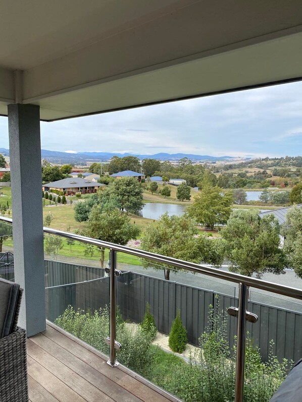 A balcony with a view of a lake, trees, and houses in the distance.