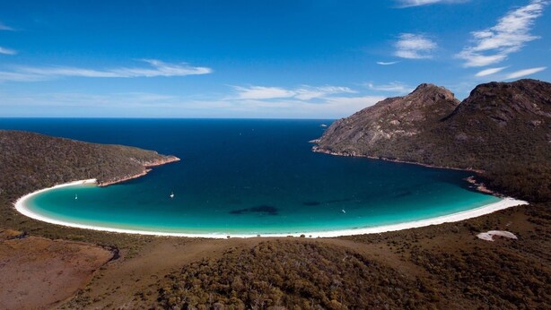 A coastal landscape with a clear turquoise bay, white sandy beach, and rugged mountains.