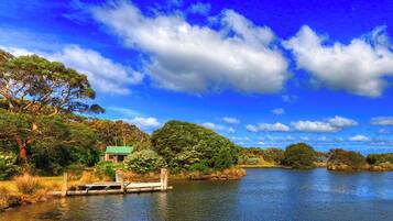 A serene riverside landscape with a wooden dock, lush greenery, and a clear blue sky.