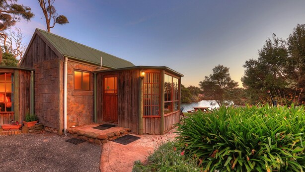 A rustic cabin with a stone exterior, a wooden porch, and a metal roof. - Stanley Lakeside Spa Cabins (Stanley)