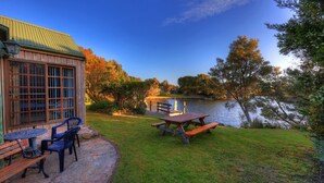 A lakeside patio with a wooden table and chairs, a stone bench, and a view of the lake. - Stanley Lakeside Spa Cabins (Stanley)