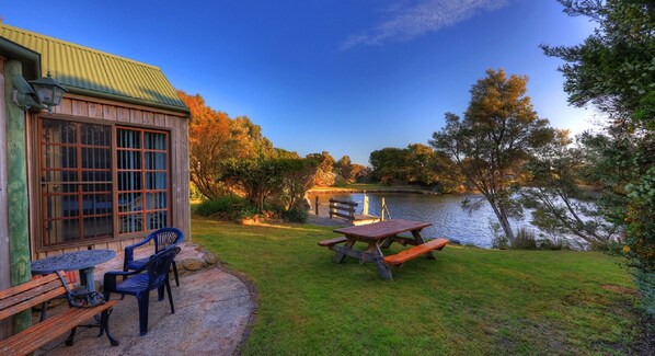 A lakeside patio with a wooden table and chairs, a stone bench, and a view of the lake. - Stanley Lakeside Spa Cabins (Stanley)