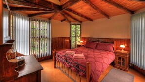 A bedroom with a wooden ceiling, a bed with a red bedspread, a nightstand with a lamp, and a window with blinds. - Stanley Lakeside Spa Cabins (Stanley)