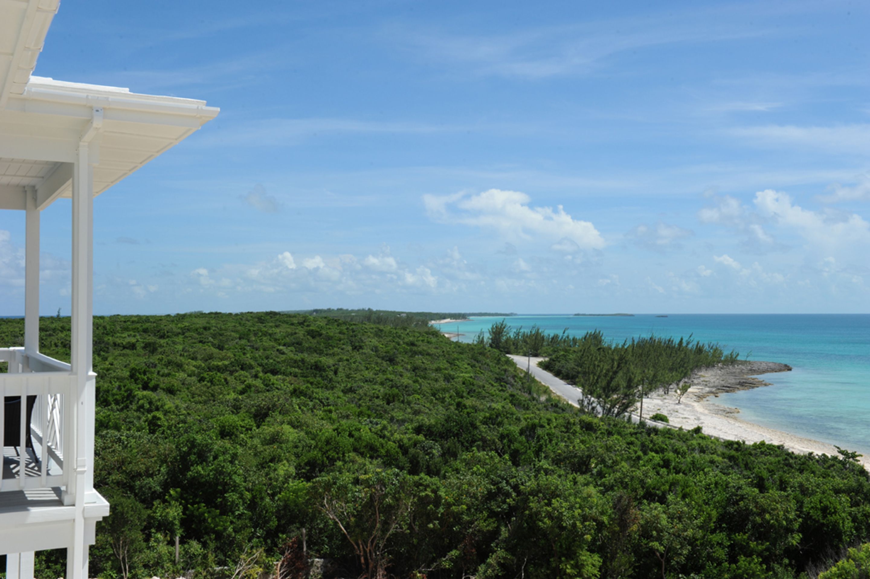 A coastal view with a white building, dense green foliage, and a clear blue sky.