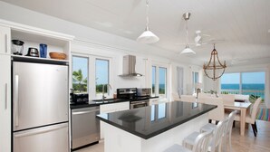 Une cuisine moderne dotée d’un grand îlot central, de meubles blancs et offrant une vue sur l’océan.