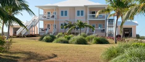 A multi-story building with a flat roof, balconies, and a well-maintained lawn with palm trees.