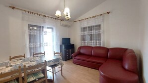 A living room with a dining table, chairs, a red sofa, and a television on a cabinet. - A family apartment close to the beach - Dara 4 (Monterol)