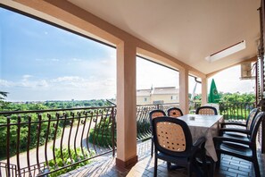 Un balcon avec une table et des chaises, donnant sur un paysage verdoyant et des bâtiments.