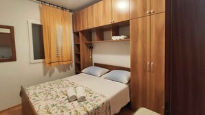 A bedroom with a bed, a wooden wardrobe, a window with curtains, and a bedside table.